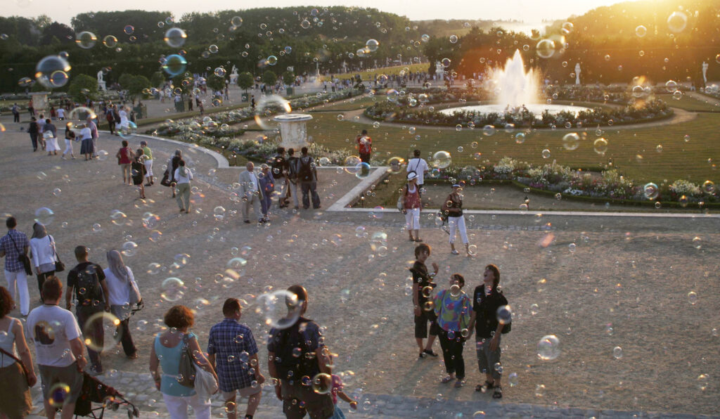 Groups of people under bubbles at sunset on the grounds of Versailles